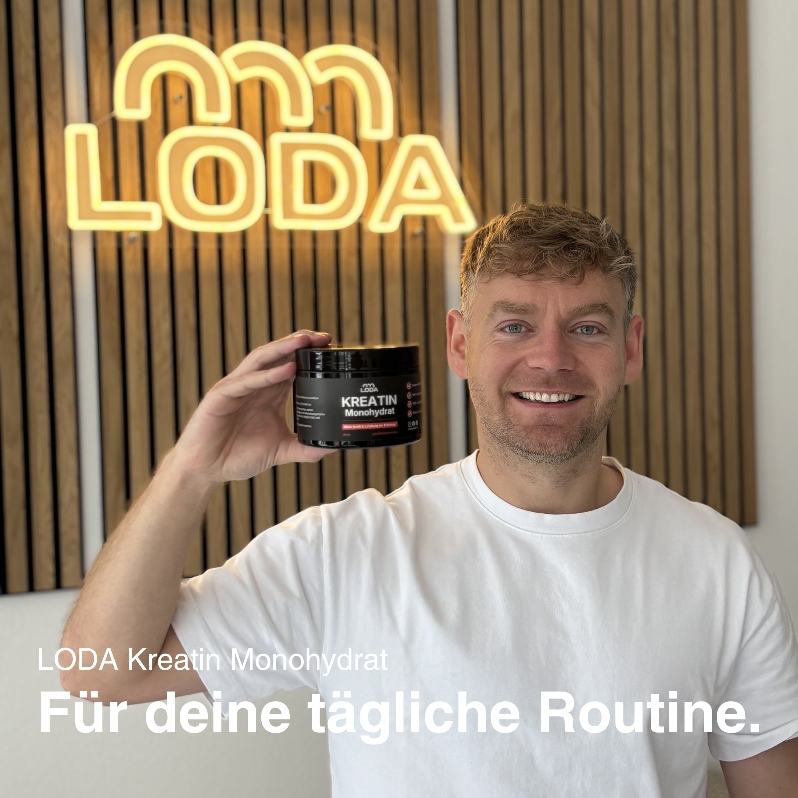 Ein lächelnder Mann hält LODA Kreatin Monohydrat von LODA sports vor einem LODA-Schild mit der Aufschrift: Für deine tägliche Routine.