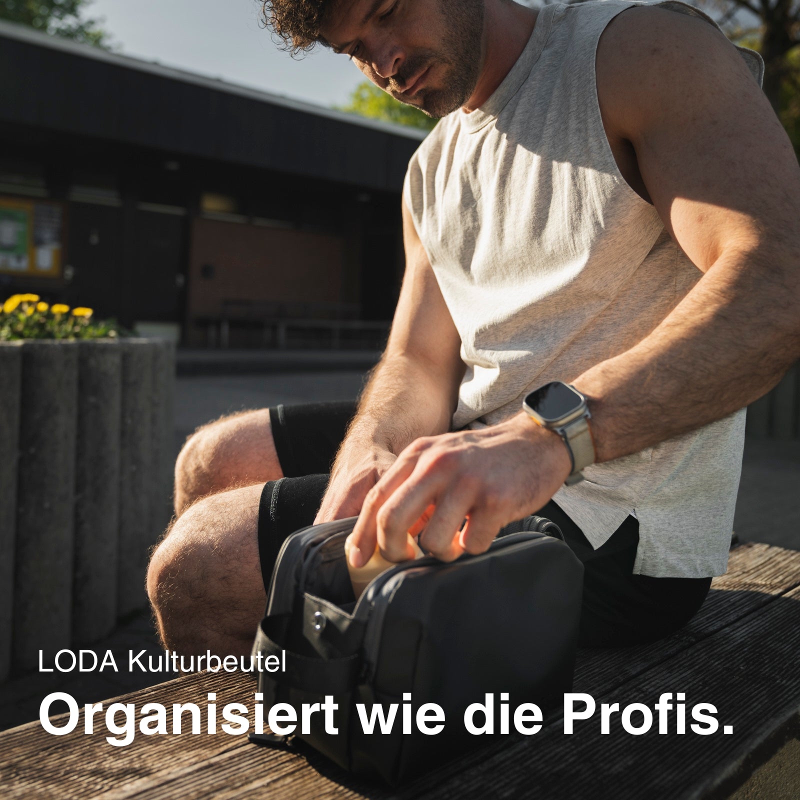 Ein Mann sitzt im Freien und packt Gegenstände in einen LODA Kulturbeutel von LODA sports. Der Text lautet: "Organisiert wie die Profis.