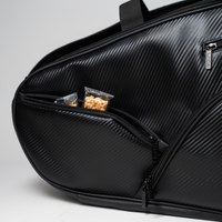 Schwarze strukturierte Tasche mit einer teilweise geöffneten Reißverschlusstasche, in der sich Snackpakete befinden.