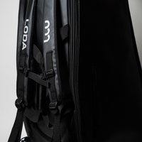 Nahaufnahme eines schwarzen Rucksacks mit LODA und weißem Logo, mit Trägern und Reißverschlusstasche vor einem einfarbigen Hintergrund.