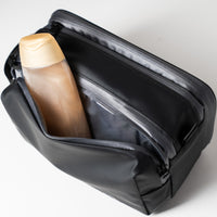 Ein schwarzer Kulturbeutel mit einer Flasche Duschgel, die teilweise in der offenen Vordertasche sichtbar ist.