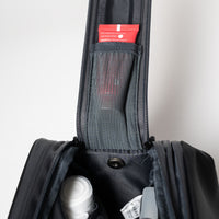 Offene schwarze Tasche mit Netztasche, in der sich ein roter Schlauch und verschiedene persönliche Gegenstände befinden, die von oben sichtbar sind.