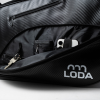 Nahaufnahme einer schwarzen Loda-Tasche mit Schlüsseln und einem Smartphone mit Doppelkamera.