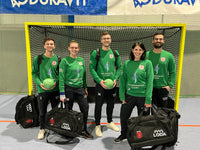 Fünf Handballspieler in grünen Trikots stehen in einer Halle vor einem Tor und halten Bälle und Sporttaschen.
